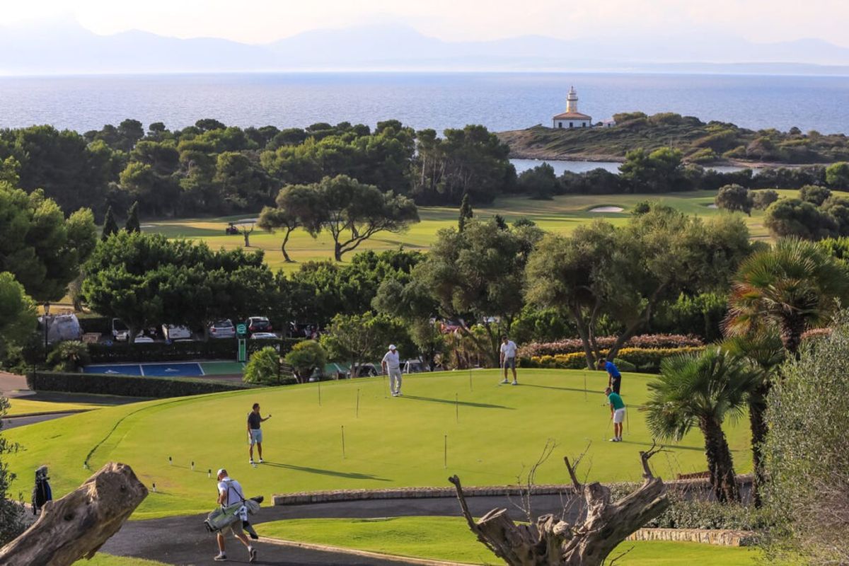 Golfer auf dem Grün mit Blick auf Leuchtturm und Bucht – Alcanada Golf, Mallorca