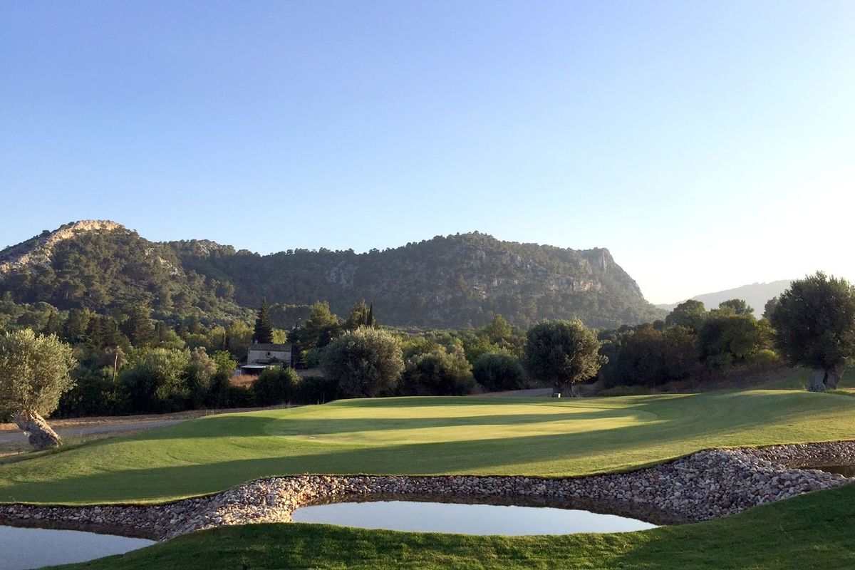 Green with a stone-walled pond and wooded hills at Golf Pollensa, Mallorca